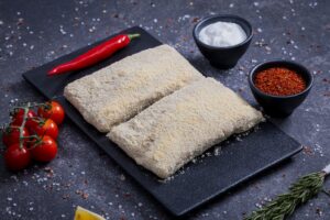 Breadcrumb-coated schnitzel portions on a slate board with cherry tomatoes and spices - The Meat Master Butchery