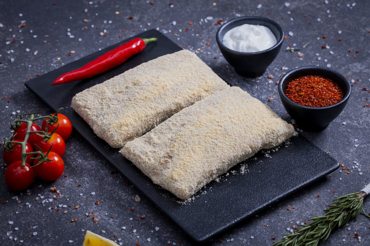 Breadcrumb-coated schnitzel portions on a slate board with cherry tomatoes and spices - The Meat Master Butchery