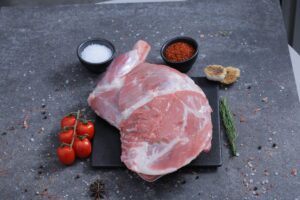 Whole raw lamb shoulder joint on a slate board with sea salt and spices - The Meat Master Butchery