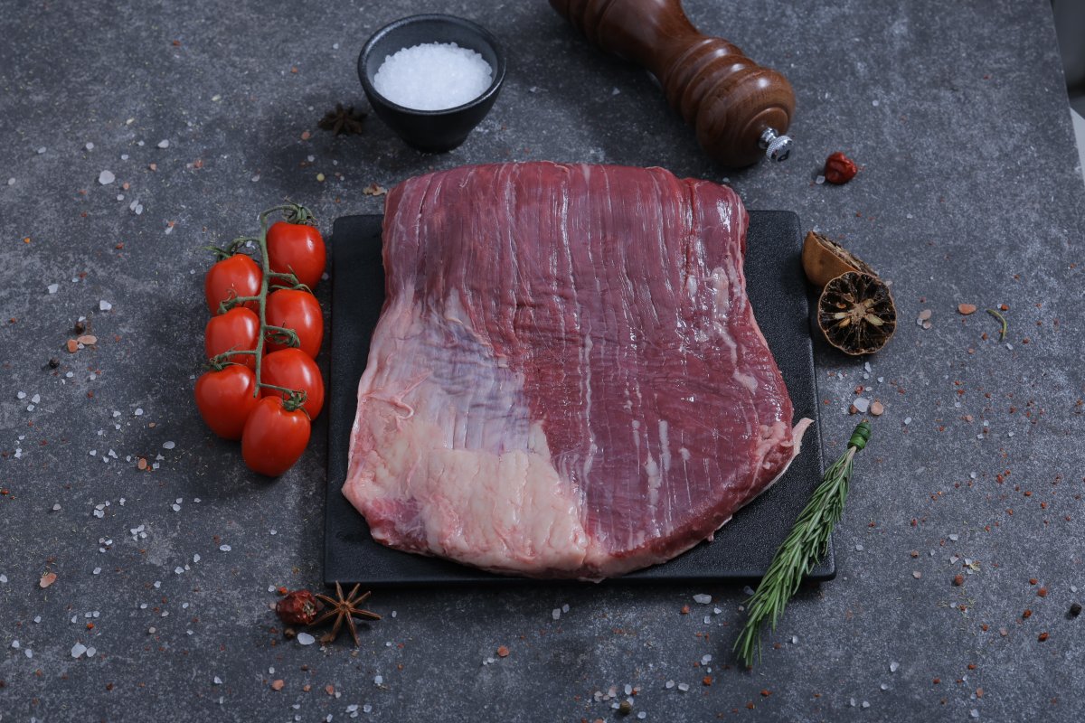 Large raw beef flank steak on a slate board with sea salt and rosemary - The Meat Master Butchery