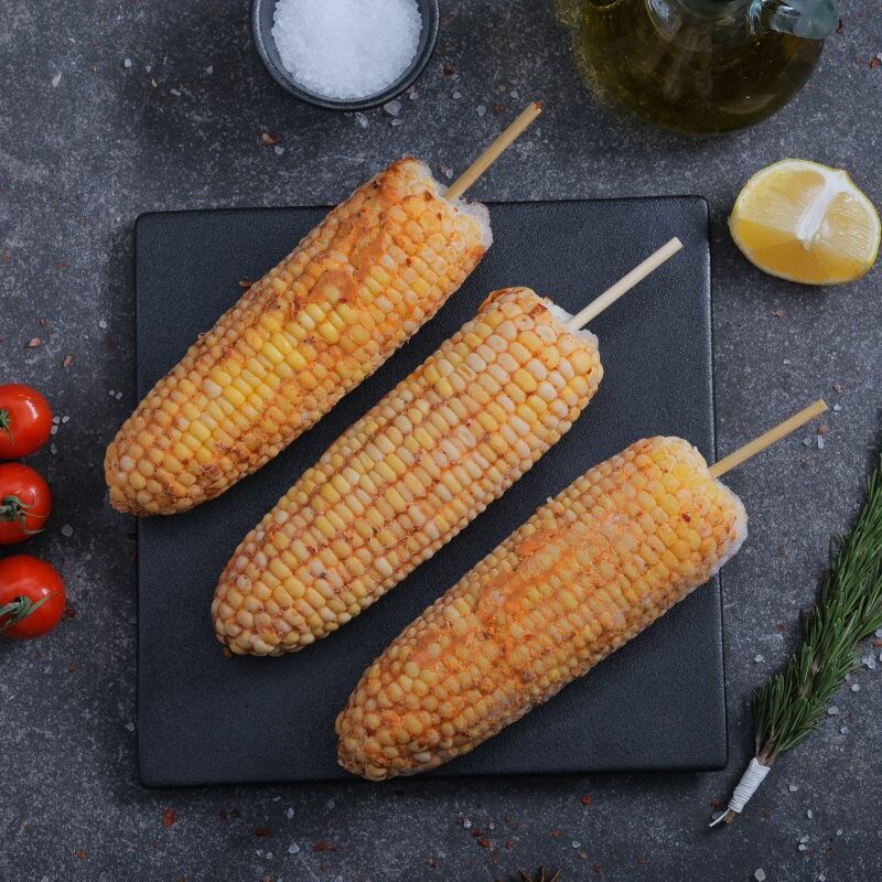 Three seasoned corn on the cob on skewers on a slate board - BBQ-ready from The Meat Master Butchery