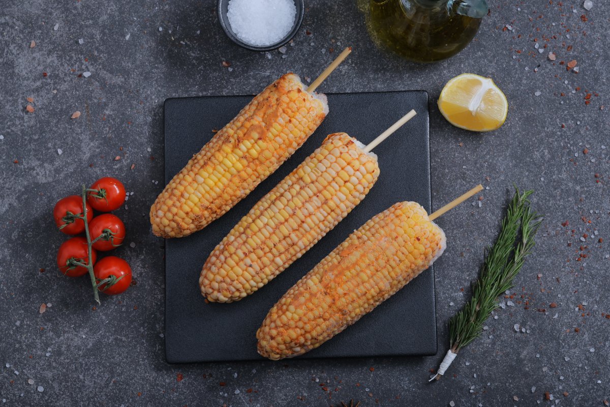 Three seasoned corn on the cob on skewers on a slate board - BBQ-ready from The Meat Master Butchery