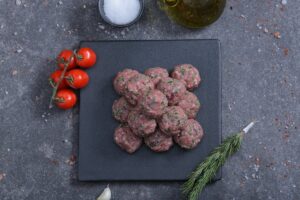 Raw herbed meatballs on a slate board with cherry tomatoes - fresh from The Meat Master Butchery