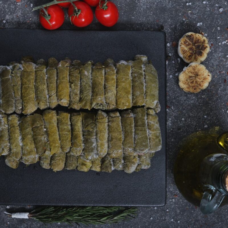 Raw stuffed grape leaves (warak enab) on a slate board with garlic and olive oil - The Meat Master Butchery