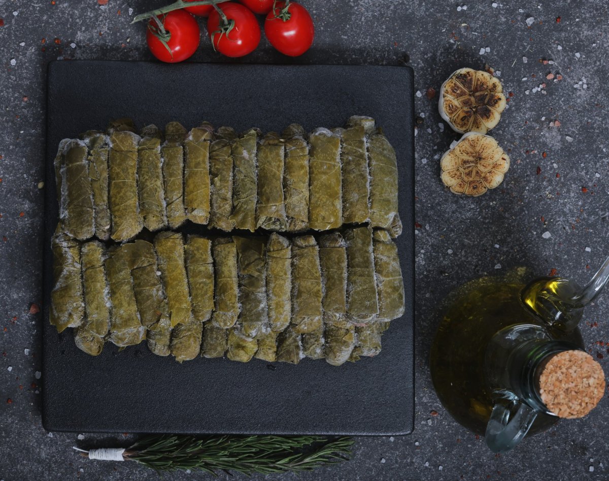 Raw stuffed grape leaves (warak enab) on a slate board with garlic and olive oil - The Meat Master Butchery